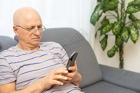 电话来了老人在用手机聊天 同时在客厅沙发上放松一下男人退休录音机微笑男性呼唤老年闲暇快乐讨论背景