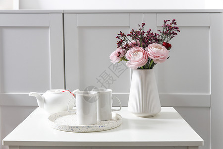 五斗柜前的白色桌子上放着一束粉红色的波斯毛茛 斯堪的纳维亚风格 放置文本花束植物框架庆典木兰草本投标茶壶卡片闲事背景图片