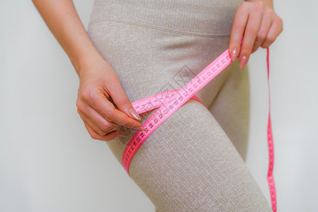 苗条女人在家里用卷尺测量她的腿的剪影 特写 一位面目全非的欧洲女性在室内检查减肥饮食或抽脂的结果 健康的生活方式腹部健身房裁剪重背景图片