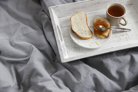 床和早餐茶壶 茶杯 两片烤面包和杏仁果酱放在床头桌子上的盘子上背景