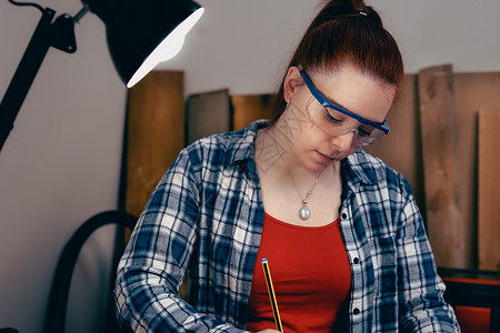 青年创业者在小生意中手工制作一块木头的手工艺品职场人士木工热情商务红发精神工作制造业眼镜背景图片