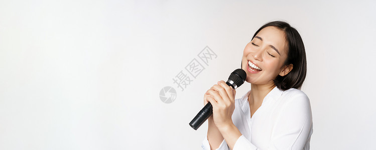 站在白色背景上 在卡拉OK的麦克风里唱着亚洲女性近距离肖像办公室卡拉ok员工成人快乐手臂冒充商务老板工作室背景图片