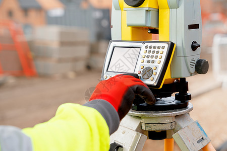 使用现代测量装备人员在房屋建筑建造工地上工作的hi-viz现场工程师;背景图片