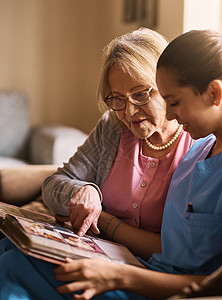 记忆力练习对他们的健康非常重要 一名护士和一名老年妇女一起看相册的镜头背景