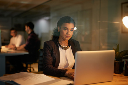 挑灯夜战 一位年轻女商务人士在办公室加班时使用笔记本电脑的镜头背景