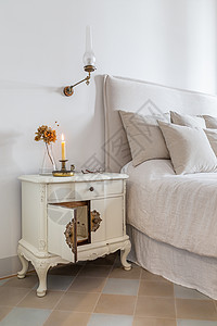 床头柜灯经典的卧室 在靠近舒适床的木制床头柜上放着燃烧的蜡烛 眼镜和鲜花 复古风格的舒适房子内部背景