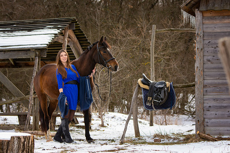 一个穿着短蓝色短裙的漂亮女孩 冬天在农场附近骑着马散步背景图片