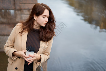 在市中心的圣彼得堡街上手握着咖啡杯 深长头发的迷人 体贴心的女人向下看 复制了空间 (Spopy space)背景图片