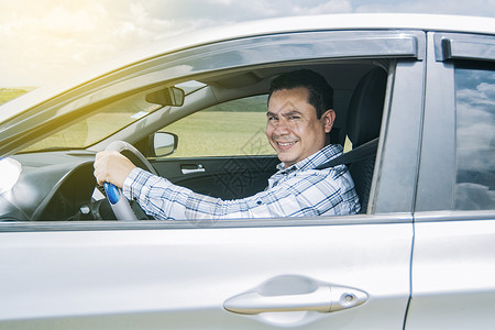 男人在他的车里对着镜头微笑 男人在他的车里开心地微笑 一个人微笑着快乐地驾驶汽车并看着相机的形象坐着高清图片素材