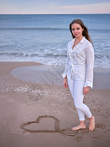 心在沙子一位身着白衣的年轻女子站在沙滩上 心跳在沙子中 看着摄像机背景