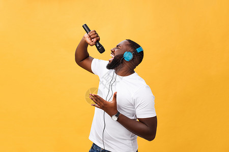 歌曲列表欢快积极 别致 英俊的非洲男子手持麦克风 头戴耳机听音乐唱歌 享受黄色背景中孤立的周末假期的肖像男人微笑寒意女性打碟机手机青少年背景