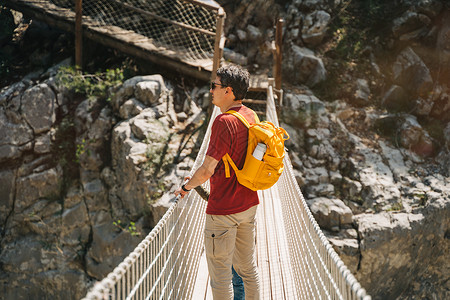 远足时 父子俩在山中的索桥上遥望 穿着随意的游客男童和他爸爸背着黄色背包穿过索桥穿过峡谷悬崖儿子天桥公园冒险石头父亲森林行人岩石木头高清图片素材