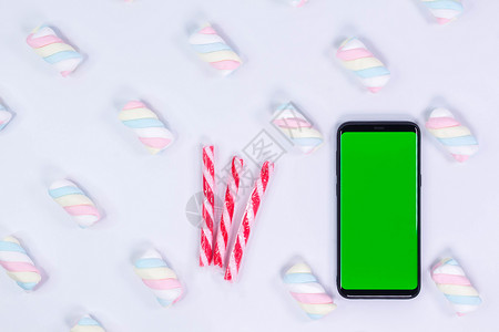 糖果样机有一个垂直的绿色屏幕的电话移动电话 拐杖糖圣诞糖果 带有扭曲的棉花糖图案的白色背景 色键智能手机技术 电话样机背景