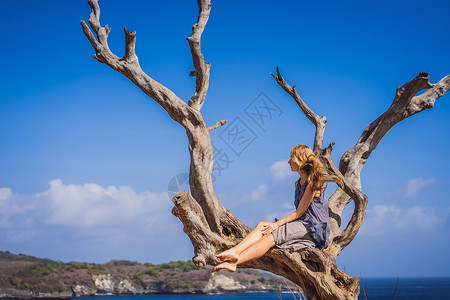 坐在树上女孩在印度尼西亚巴厘岛努沙佩尼达的海天使比拉邦背景下坐在树上的妇女 巴厘旅行概念墙纸海岸自由海洋旅游海滩岩石游客成人海岸线背景