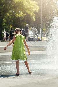 水流中孩子在公园喷泉前穿绿衣的赤脚女孩 高水流 在炎热的夏季日子里给儿童带来乐趣女性城市阳光活动喜悦快乐幸福孩子娱乐青年背景