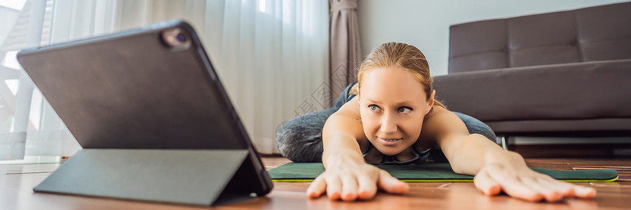 健身女性在家里的地板上锻炼 并在平板电脑上观看健身视频 人们因为冠状病毒而在网上做运动横幅 长格式重量公寓成人训练肺炎互联网影片背景图片