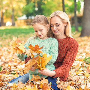 女人和叶子持有秋天黄叶的妇女和女童微笑女儿叶子女士童年活动快乐乐趣情绪森林背景