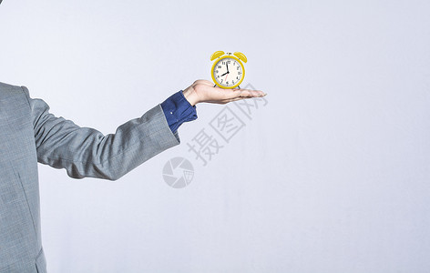 一个黄色的闹钟一只手在孤立的背景下拿着一个台钟 一只手拿着闹钟的特写 商务人士手拿着一个孤立的时钟背景