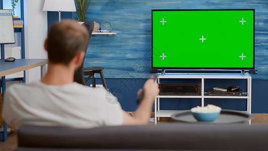在电视上观看绿屏时 男子在静态三脚手拍换频道的画面男人高清图片素材