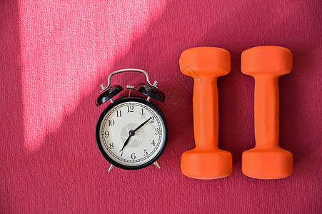 两条橙色隧道和一张粉红色瑜伽垫上的闹钟 该用设备在家健身了 检疫体育纪律培训师瑜伽身体运动健身房重量有氧运动损失警报力量背景图片