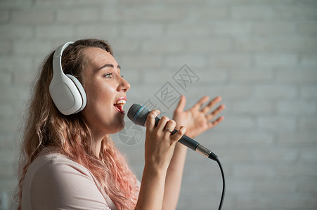 耳机带字素材穿着白色耳机的美丽情感女孩在家中卡拉OK唱着一首歌 并积极向砖墙做手势 在电视上 她写道 我最喜欢听一个字演员嘴唇卡拉ok麦克风背景