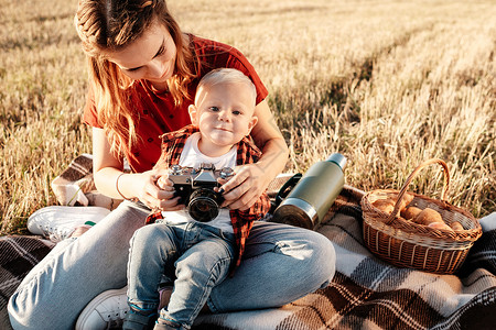 快乐的妈妈和她的小儿子在阳光明媚的日落时分在城外的田野里享受夏日周末母性公园相机孩子儿子男生场地女性投标婴儿背景