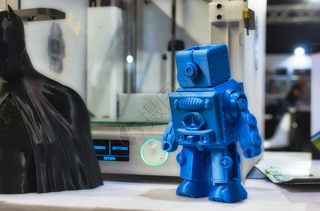 小蓝色背景3D 打印机器人模型 与一个技术和工具展览会的3D打印机相邻塑像玩具造型工业生产材料印刷创新蓝色展示背景