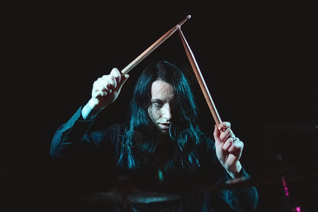 一只长发的女金属鼓手 在黑暗背景下将鼓棍握在鼓声背后背景图片