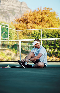 专业人士总是准备充分 一个运动型的年轻人在网球场上系鞋带的镜头背景
