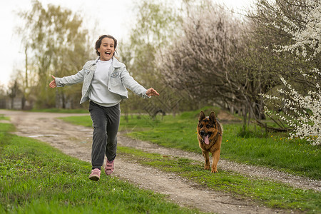 小女孩带着狗在花花园里跑步童年孩子动物娱乐微笑猎犬友谊朋友公园街道树高清图片素材