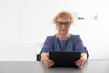 快乐成熟的中年女性在家里使用数字平板电脑度过闲暇时光 性格开朗的现代高级女士拿着电脑 看有趣的电影和笑声 休闲和科技理念会议奶奶祖父母高清图片素材