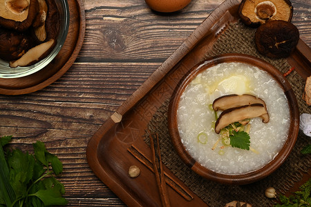 传统的中国大米粥 配有蘑菇 软煮蛋 姜切片和木制桌上的炒肉背景图片