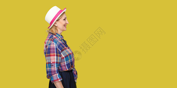 时尚的中年妇女 在黄色背景下从事临时作风金发女郎牙齿奶奶老年化妆品皮肤护理成功帽子衬衫背景图片