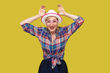时尚的中年妇女 在黄色背景下从事临时作风享受女士衬衫女性耳朵幸福乐趣祖母示范老年背景图片