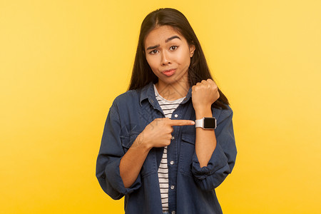 黄色背景的年轻亚洲女人的肖像焦虑小时女性警告手腕女士手指老板检查女孩钟高清图片素材