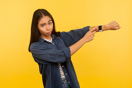 黄色背景的年轻亚洲女人的肖像手腕女士手指老板手势女孩女性手表小时检查东南高清图片素材