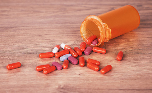 一瓶打开的橙色药丸洒在一张木桌上 维生素补充剂是保持健康的好方法 慢性病和处方药通常由医疗救助覆盖背景图片