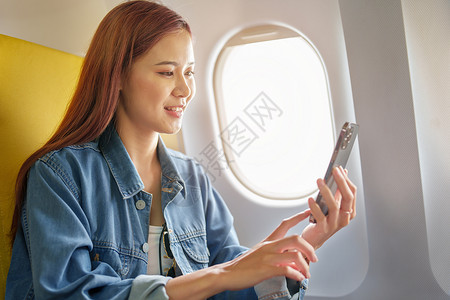 等飞机女人坐在经济舱靠窗座位的亚洲女性在机上 旅行概念 假期 放松时使用手机的迷人肖像女士运输商业旅游飞机背包航空公司乘客游客班级背景