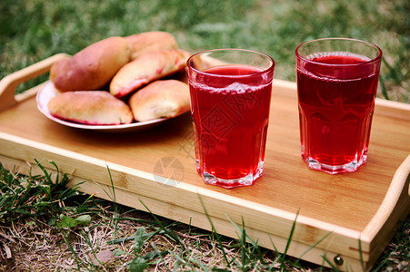 美味的自制樱桃馅饼和两杯喝的莓果酒 在花园草坪上的托盘上背景图片