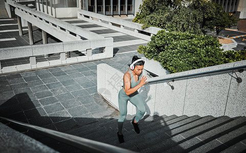 年轻的混血女运动员戴着耳机听音乐 在城外跑上楼梯 锻炼有益于您的健康和幸福背景