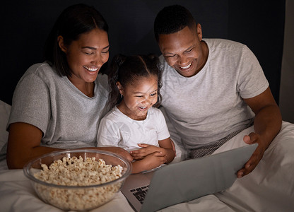 家庭电影之夜对我们来说很重要 一对年轻夫妇和女儿一起坐在床上 晚上用笔记本电脑周末高清图片素材