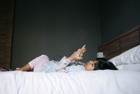 坐在床上的在智能电话上看漫画的女孩背景图片