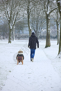 父亲和儿子带着雪橇在雪雪中行走降雪公园孩子背景图片