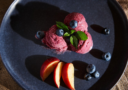 冰淇淋菜单在海军盘子上刷新素食的黑莓糖 上面沾满了薄荷叶 蓝莓和多汁桃子背景