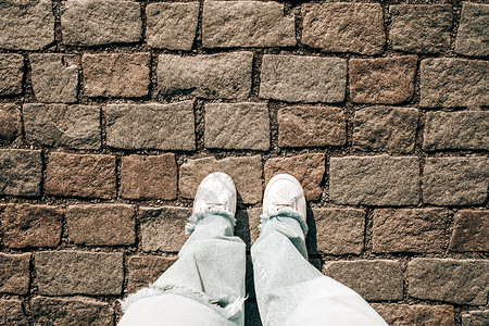 穿着牛仔裤和白色运动鞋的女性腿在铺路石上 十几岁的脚顶视图 布拉格街道 老城区路面高清图片素材