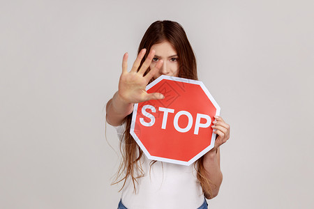 严厉的女人愤怒地看着 表现出停止的姿态 举着道路交通标志作为禁令的警告背景图片