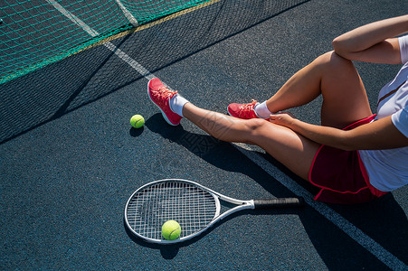 一个穿着运动裙的无脸女孩坐在网球场上 拿着一枚火箭 对女性腿最有洞察力少年闲暇活动运动服运动员女士行动体育锻炼球拍晴天背景图片