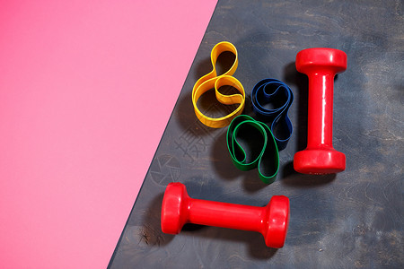 红色哑铃和松紧带 用于粉红色背景的运动 健康的生活方式 重量训练的健身器材 肌肉发育和健身训练瓶子瑜伽橡皮乐队力量女孩活动横幅身背景图片