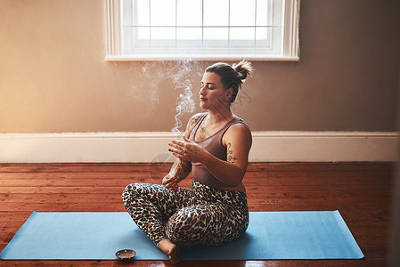 一位年轻女子在家坐在瑜伽垫子上 烧了一只巴罗桑托棍子的火葬场 他写道背景图片