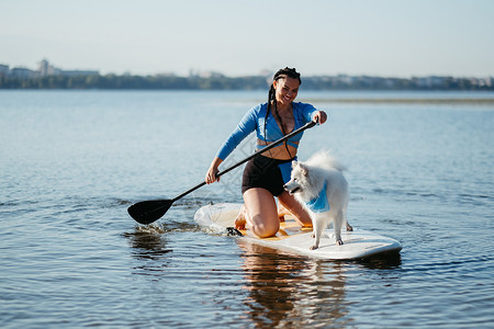 划船的女孩在城市湖的Sup委员会 和她的狗 白雪白日日式日本人史匹兹一起划船背景